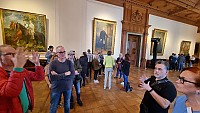 Die Gruppe der Teilnehmerinnen und Teilnehmer bei einer Führung durch die Villa in einem großen Saal, in dem verschiedene Gemälde an den Wänden hängen.