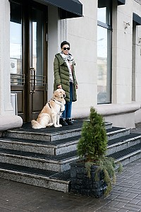 Eine blinde Frau steht mit einem Hund auf dem Podest einer 4-stufigen Treppe vor einem Haus
